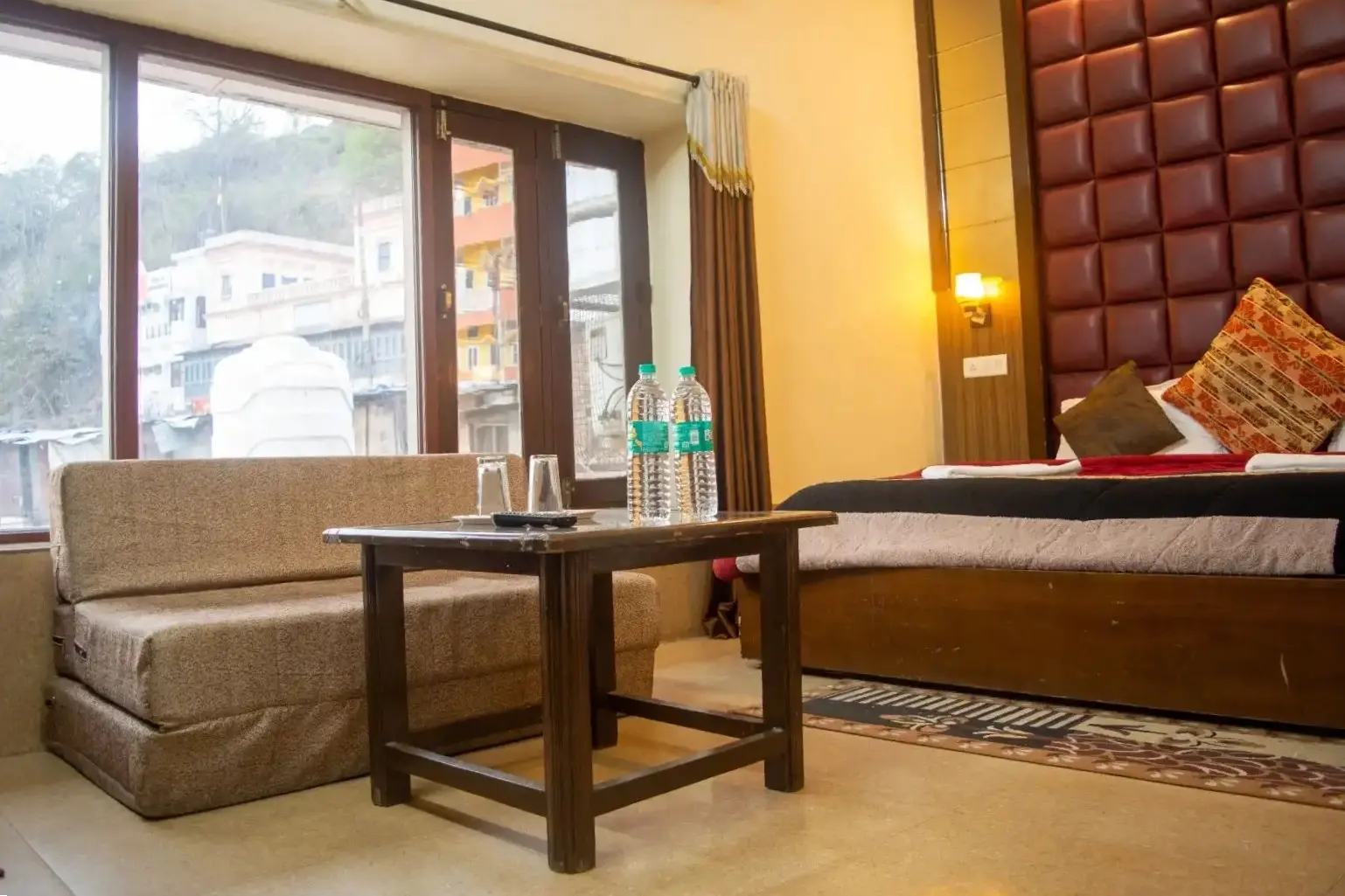 Hotel room seating area in Haridwar with sofa, table and large window view